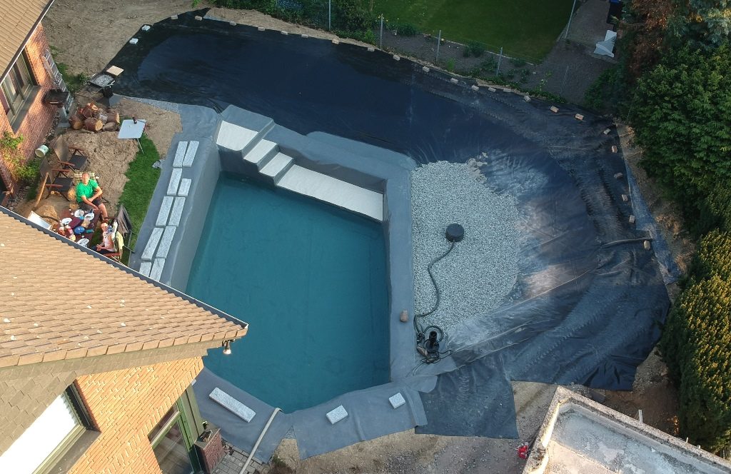 Luftbild des Schwimmteichs im "Schwimmteich Bau Bautagebuch" von Mielke's Naturbadeteich. Das Drainagesystem ist mit Kies bedeckt, und die Folie überlappt für die Kapillarsperre.