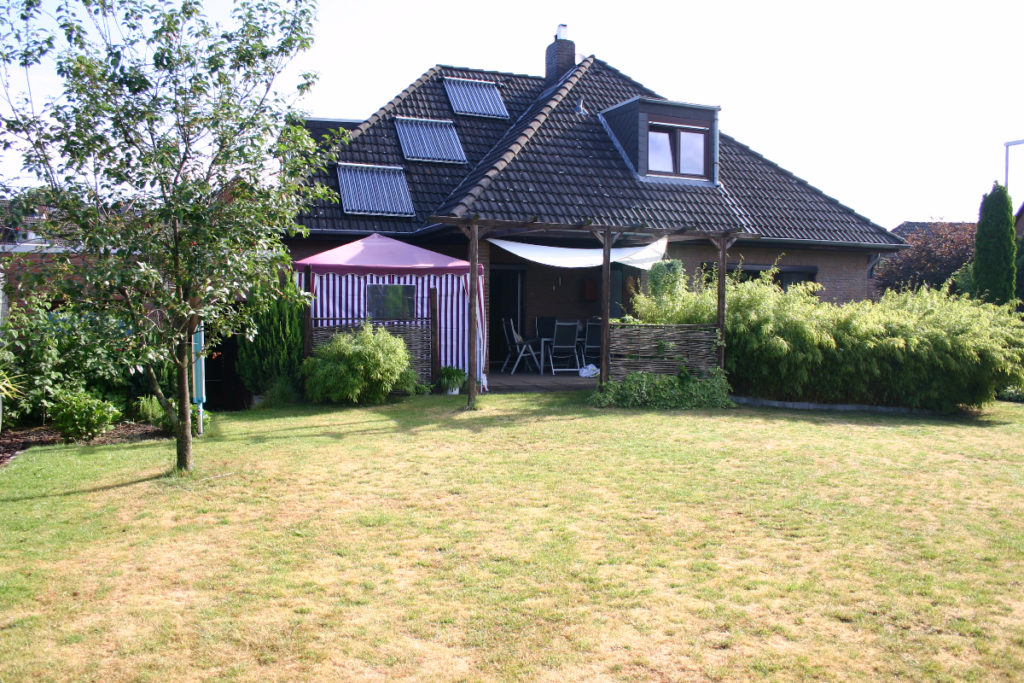 Idyllische Wiese mit Baum und Haus mit Terrasse