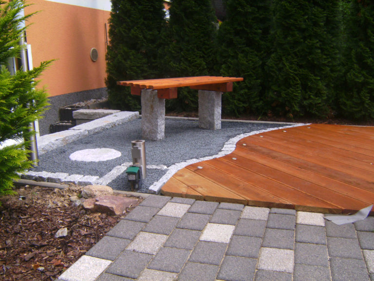 Sitzecker mit einer Bank gebaut aus Granit und Holz. Terrassenbohlen mit eingelassener Beleuchtung