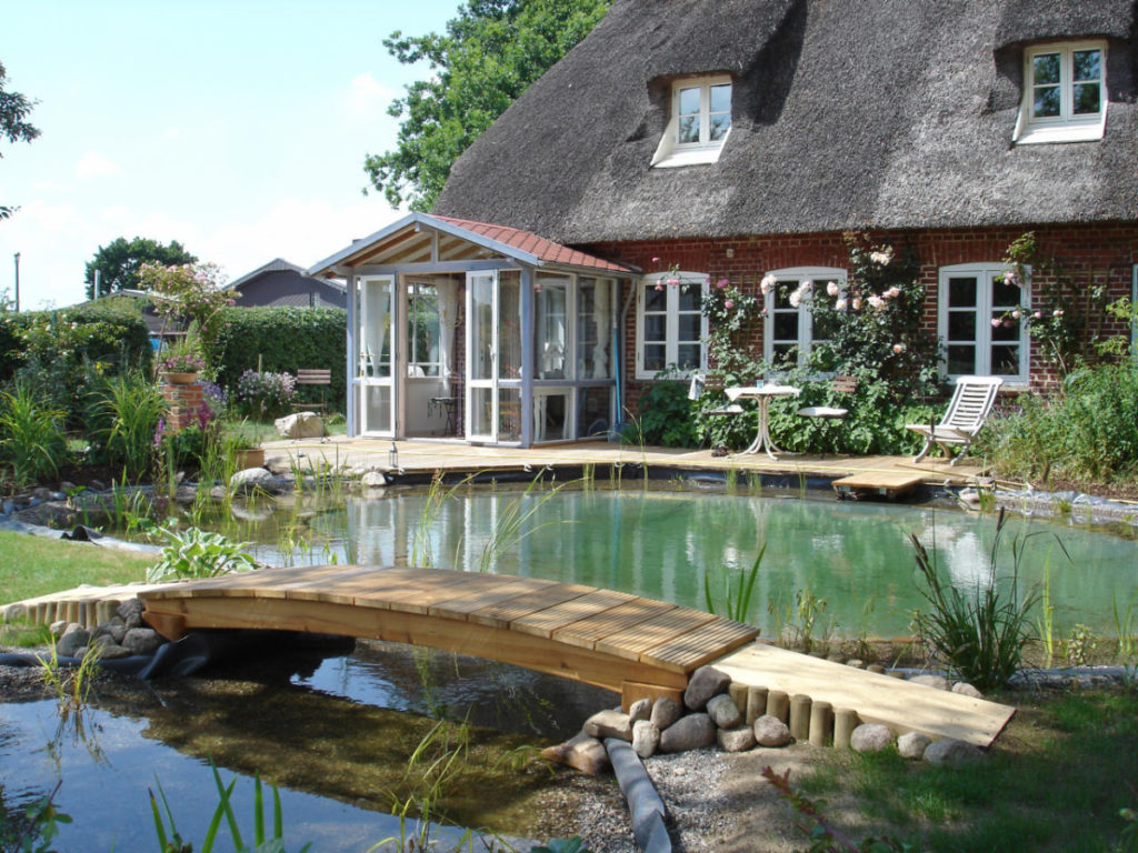 Eine kleine Holzbrücke führt über den Schwimmteich bei Flensburg