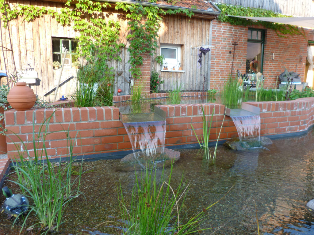 Höher gelegener Pflanzenbereich an einer Terrasse der Überlauf ist ein Wasserfall der in den Schwimmteich führt