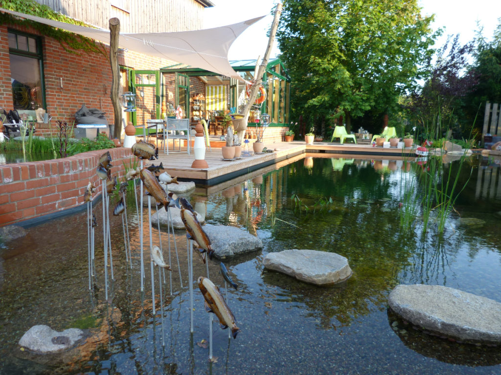 Trittsteine im Pflanzenbereich dekoriert mit kleinen Fischfiguren die aus dem Wasser springen und wieder eintauchen