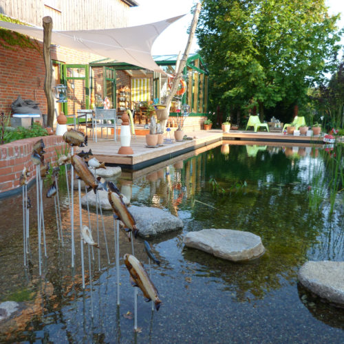 Trittsteine im Pflanzenbereich dekoriert mit kleinen Fischfiguren die aus dem Wasser springen und wieder eintauchen