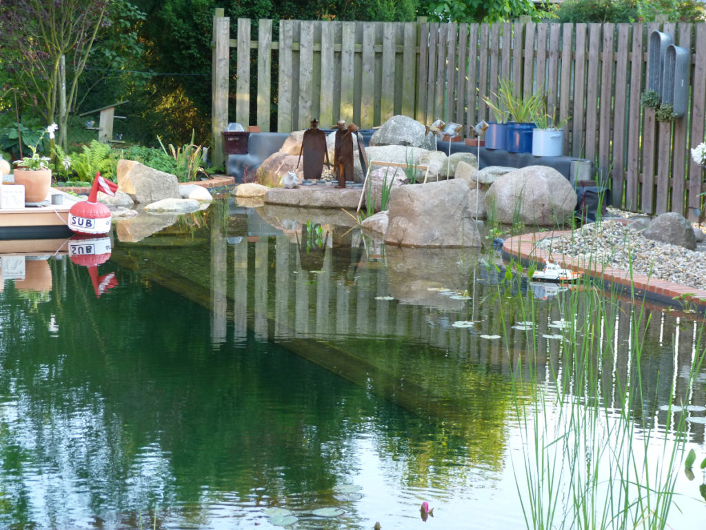 Verschmelzung von Teich und Kunsthandwerk. Kleine Pinguin Rostfiguren, eine Boje und viele weitere Dekoelemente