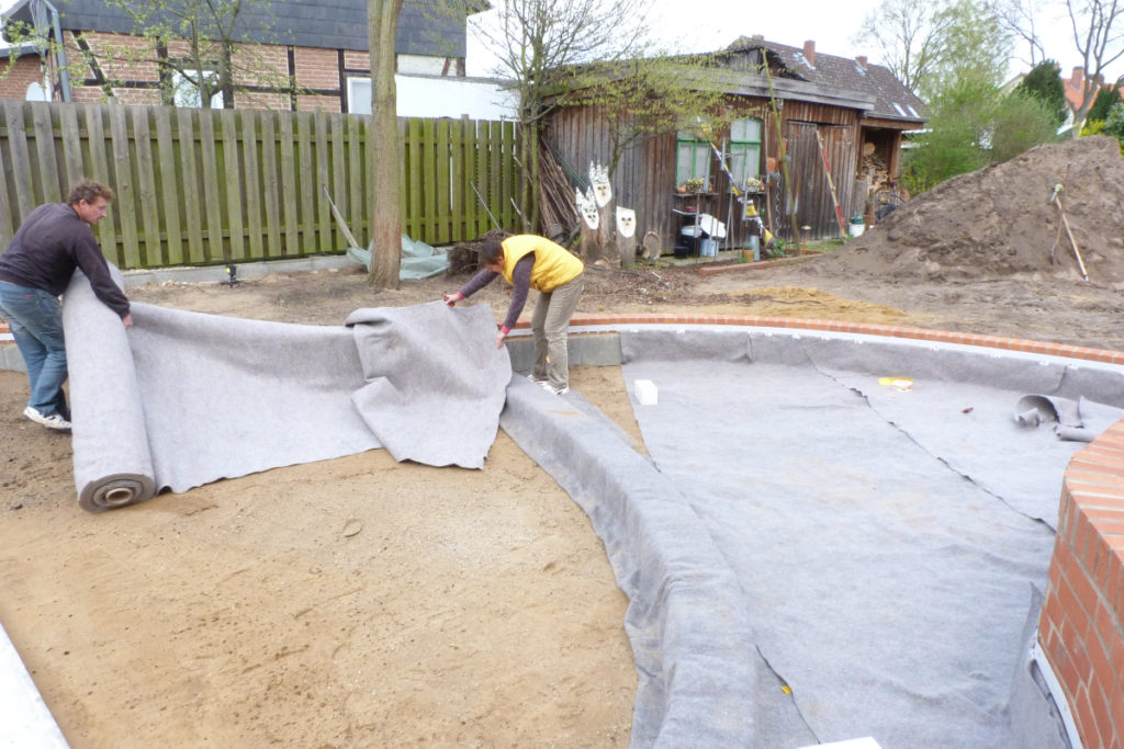 Mitarbeiter legen Vlies im Pflanzbereich eines Selbstbau-Schwimmteichs in Gifhorn, Niedersachsen.