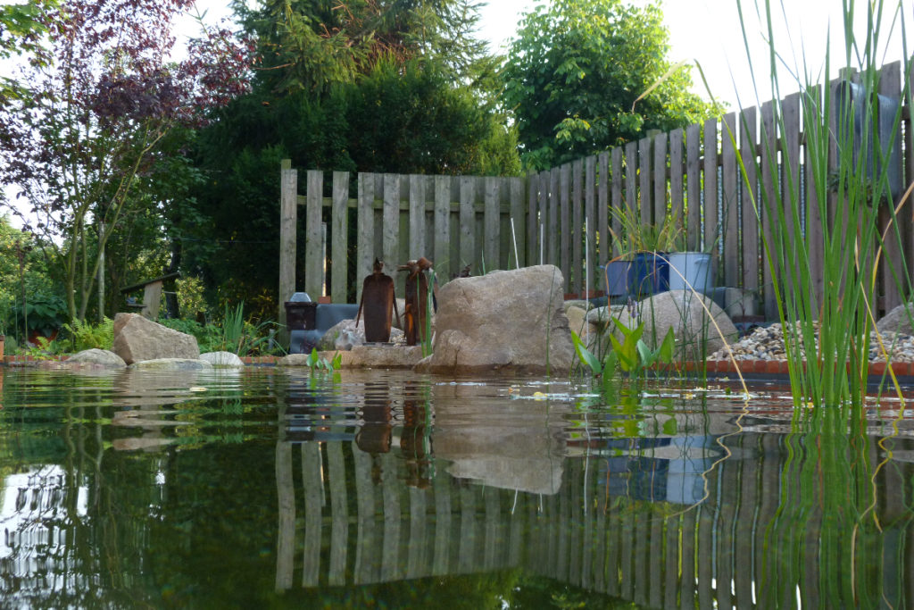 Ecke des Pflanzbereichs mit Findlingen und Figuren dekoriert in einem Selbstbau-Schwimmteichprojekt.