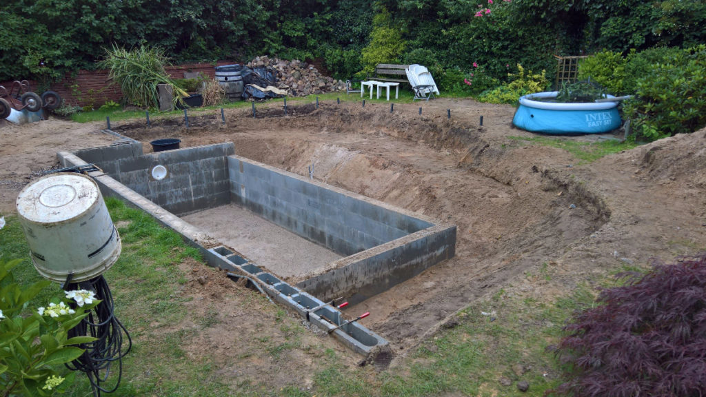 Der Schwimmbereich wird gemauert, während eine U-förmige Filterzone ausgehoben wird.