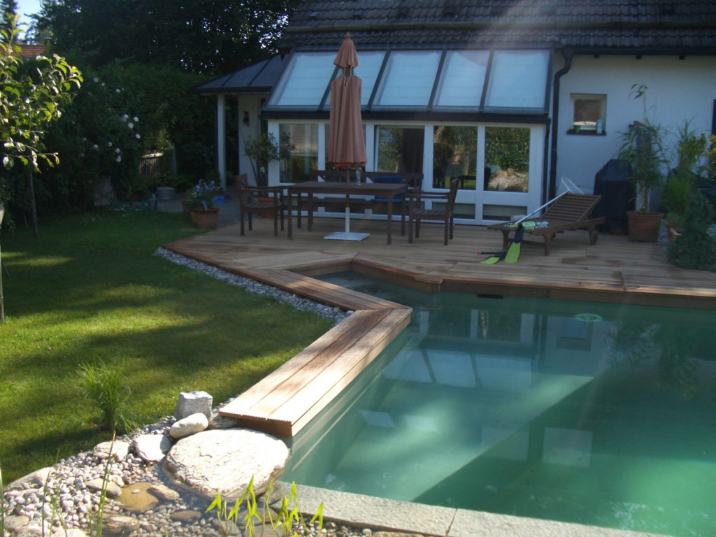 Eine Holzterrasse und gleichzeitig Sitzfläche umgeben den Schwimmbereich des Teiches