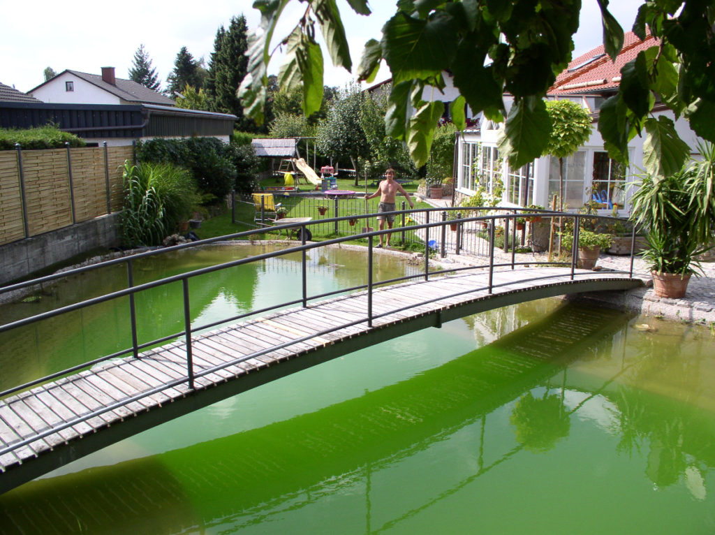 Hier wurde eine große Brücke aus Stahl mit Holzbrettern über den Schwimmteich gebaut