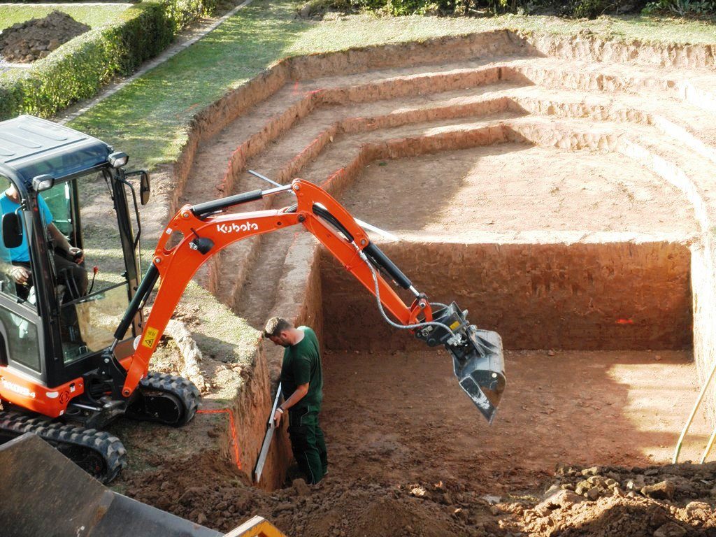 Bagger baggert den Teich. Pflanzzone treppenförmig rund. Schwimmbereich übergehend rechteckig.