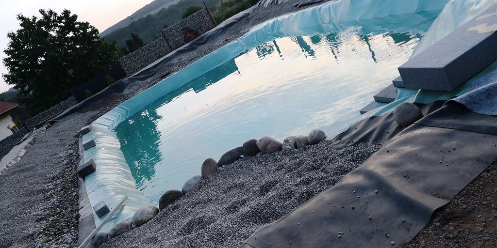 Der Schwimmbereich ist vollständig mit Wasser gefüllt, der Pflanzbereich ist mit Kies gefüllt, und auf den Treppenstufen liegen Steinplatten.