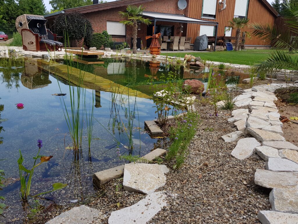 Liebevoll dekorierter Schwimmteich mit vielen Natursteinen Terrasse Strandkorb und Windmühle