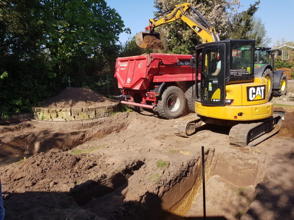 Schwimmteich-Baustelle - Ein Bagger gräbt die Teichmulde und ein LKW fährt den Aushub ab.