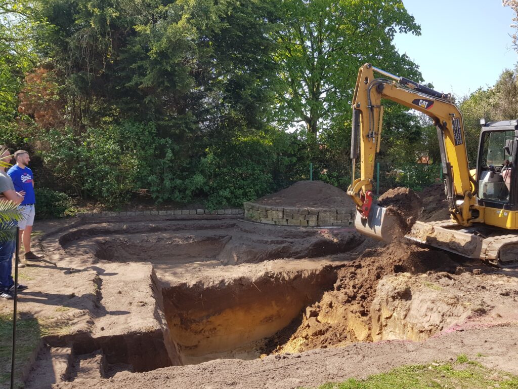 Bagger hebt Erde für Schwimmbereich aus, teilweise ausgehobene Pflanzzone