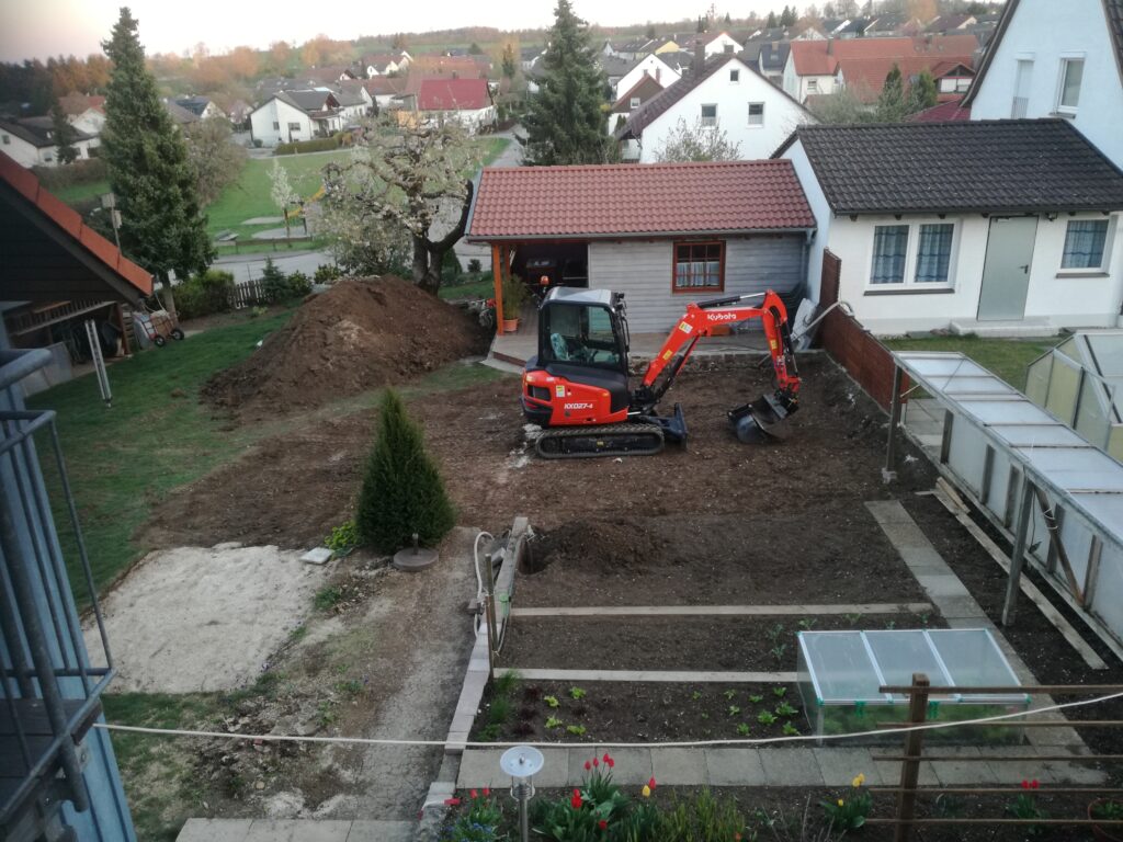 Minibagger beginnt mit dem Erdaushub vor dem Holzhaus – Ein entscheidender Schritt im Schwimmteich Selbstbauprojekt.