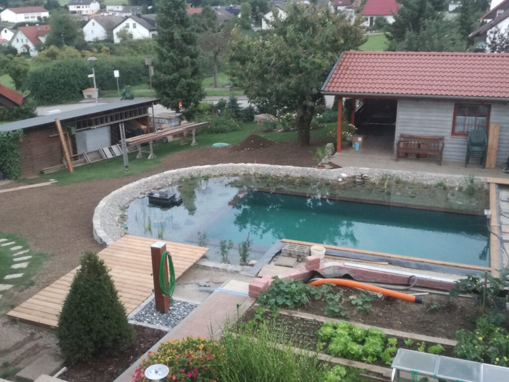 Blaues Wasser und Holzterrasse am Schwimmteich – Einladender Ort zur Erholung im Garten.