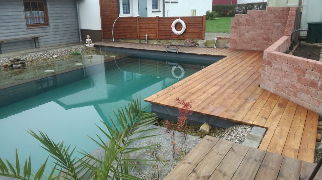 Holzterrasse und Ziermauer am Schwimmteich – Liebevolle Details im gestalteten Garten.