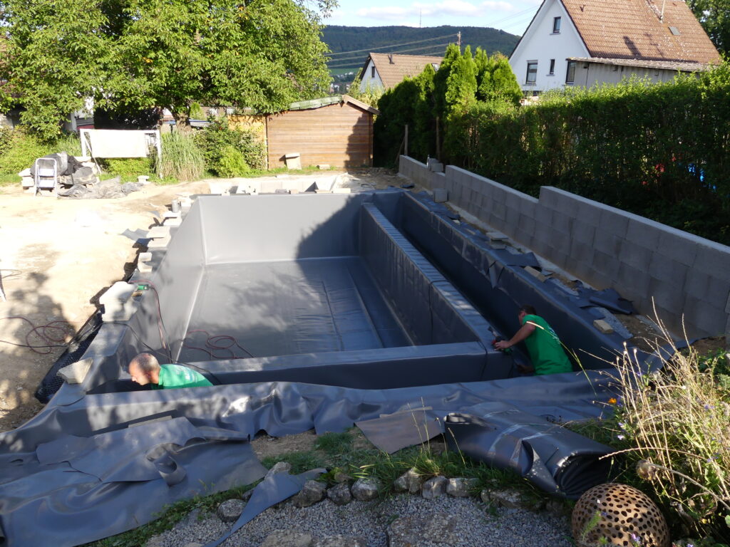 Verschweißen der Folie im Schwimmbereich, Anpassung an die Mauer, Mitarbeiter verschweißen die Folie.