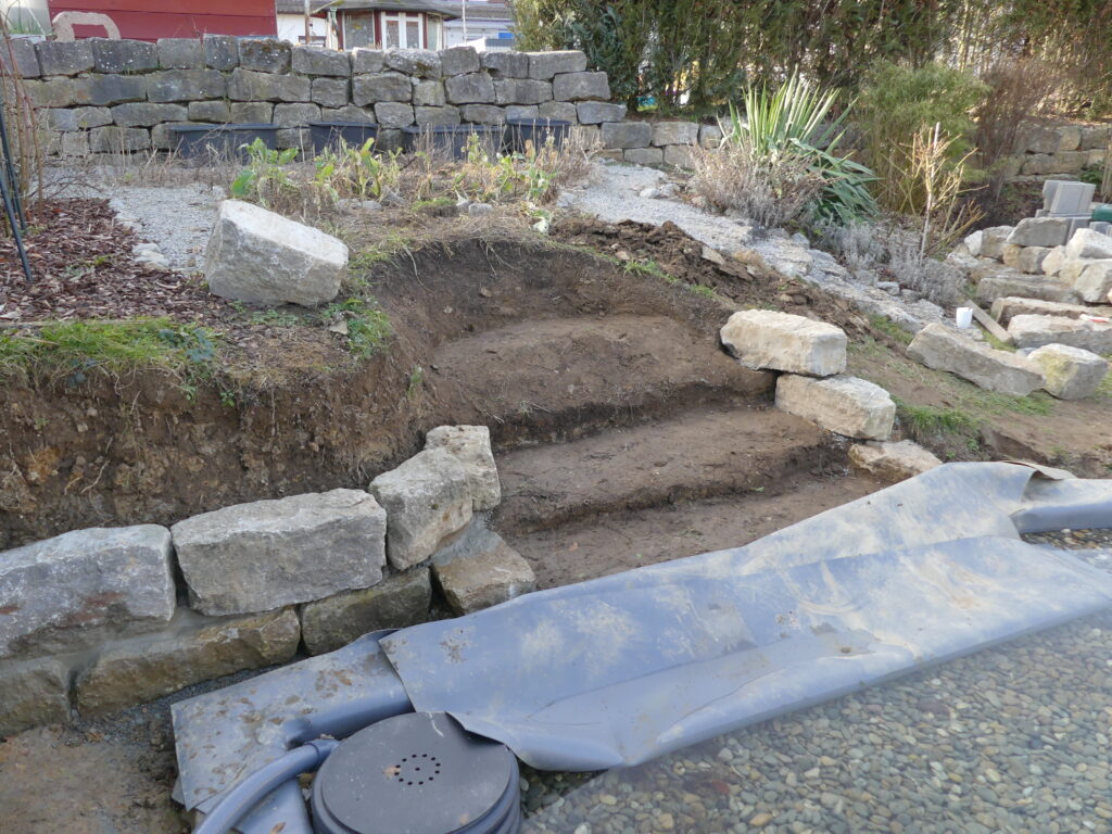 Erdgeformte Treppenstufen, Steinmauer, Drainagetopf neben der Treppe.