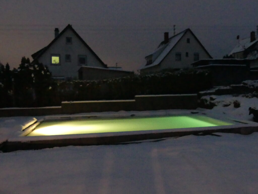 Verschneiter Naturpool im Winter, das Wasser leuchtet grün