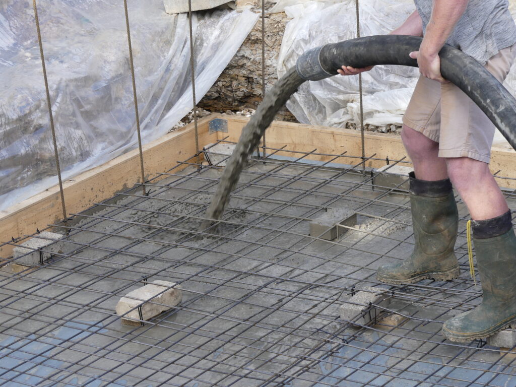 Vorbereitung des Bodens mit Holzrahmen und Folienabdeckung, Gießen von Beton, Armierung auf Steinen.