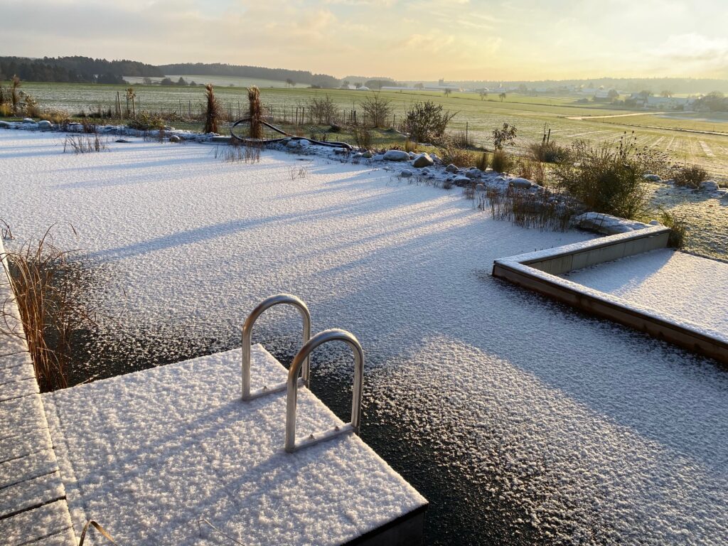 Der Schwimmteich im Winter, eingehüllt in eine zauberhafte Schneedecke, mit einer friedlichen Ruhe, die die Natur umgibt.